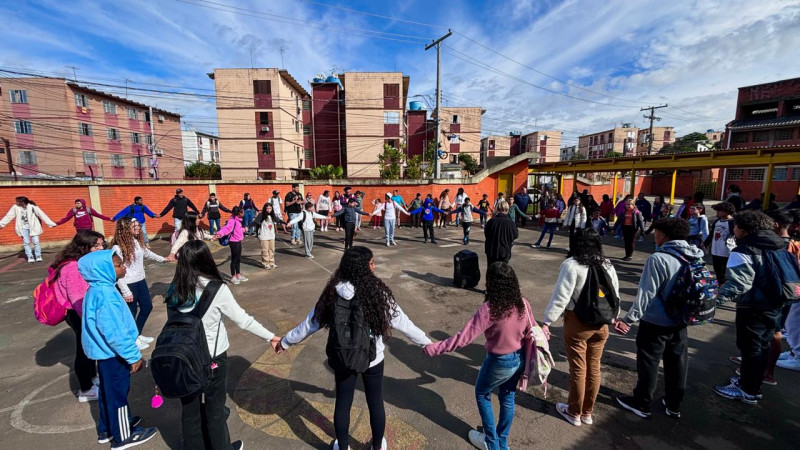 Foto de um dia ensolarado no pátio da Escola Ensino Fundamental Júlio Barelli, onde crianças estão reunidas em um círculo, numa atividade de acolhimento.