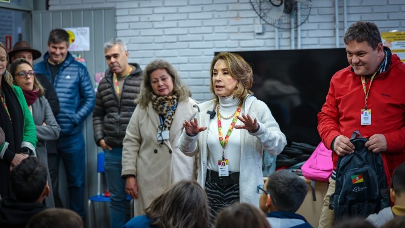 Foto tirada numa sala de aula do Centro Esportivo Sesi Rubem Berta. A secretária de educação, Raquel Teixeira, está no centro da cena. Ao redor, estão as crianças que atendem às aulas no abrigo do local