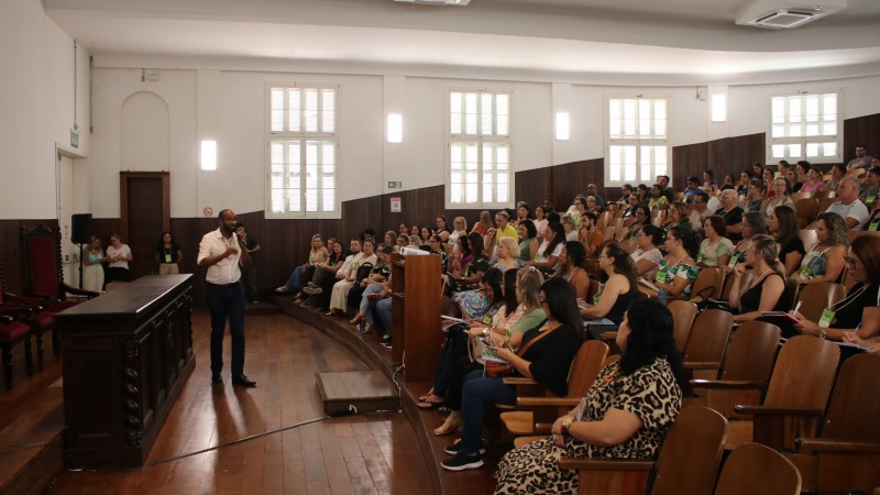 Foto do auditório do Instituto de Educação, em Porto Alegre, onde uma plateia de professores escuta o subsecretário de desenvolvimento da educação, Marcelo Jerônimo, que segura um microfone próximo a uma mesa de madeira.