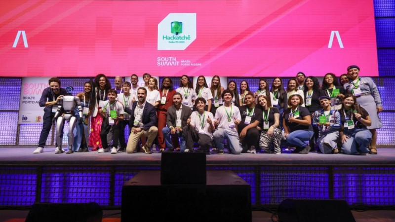 Foto do palco do South Summit, com o governador Eduardo Leite e o vice-governador Gabriel Souza ao centro, rodeados pelos estudantes das equipes finalistas do HackaTchê Business