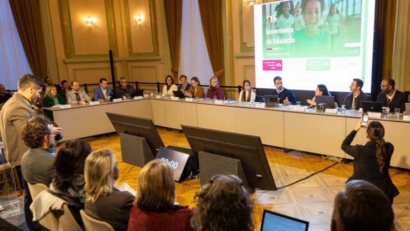 Grupo de trabalho reunido em torno de uma mesa de conferência no Palácio Piratini, com a presença do governador Eduardo Leite. Uma tela exibe a apresentação "Governança da Educação". Há laptops e microfones sobre a mesa.