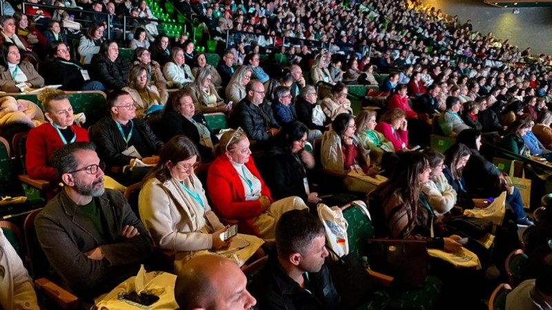 Auditório lotado com centenas de pessoas sentadas, todas voltadas para o palco, assistindo atentamente a uma apresentação. A iluminação foca no público da frente, e muitos usam crachás, indicando participação no Seminário da Secretaria da Educação.