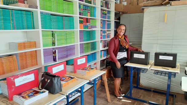 Na imagem, uma mulher aparece ao lado dos espa&ccedil;os de vota&ccedil;&atilde;o, em um ambiente escolar, sorrindo e posando para a voto ap&oacute;s depositar sua c&eacute;dula