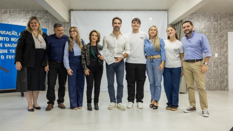 Registro coletivo em ambiente interno, com um grupo alinhado lado a lado para foto institucional. O governador ao centro segura um documento, indicando ato formal de entrega.