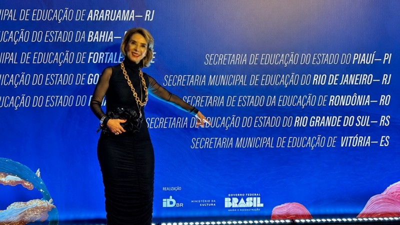 Raquel Teixeira posa sobre tapete vermelho diante de painel azul do Pr&ecirc;mio Sim &agrave; Igualdade Racial 2026. Ela aponta para o nome da Secretaria da Educa&ccedil;&atilde;o do Rio Grande do Sul, listado entre os finalistas da categoria Educa&ccedil;&atilde;o.
